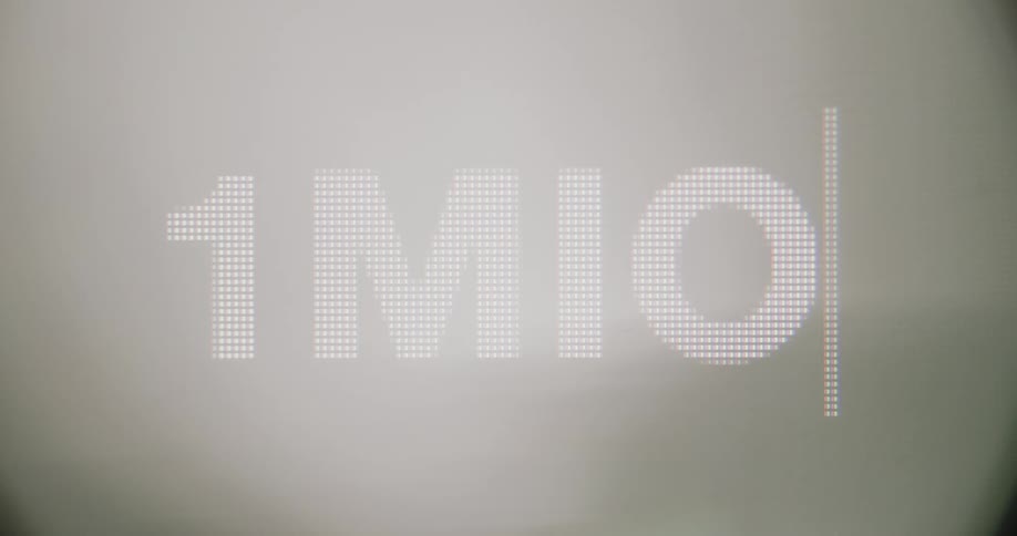 The text 1mio is displayed using a pixelated font against a hazy light background