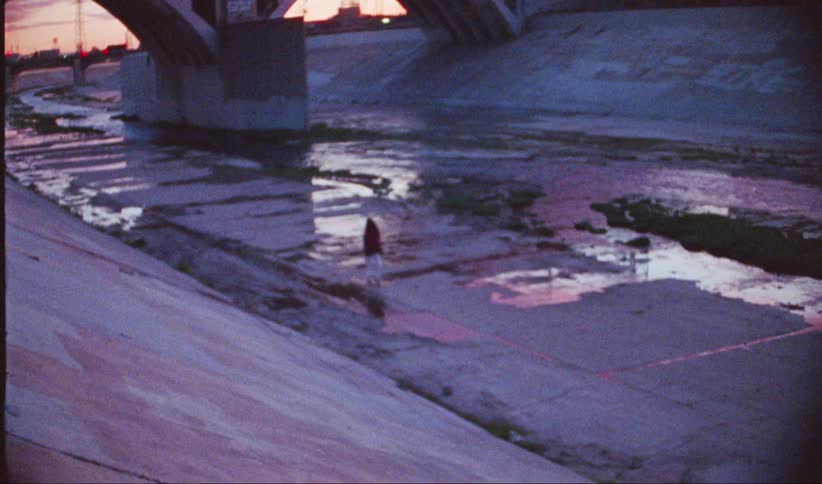Woman walking below an overpass with water flowing