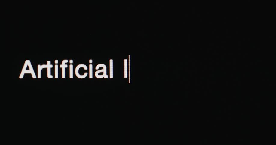 Close up of the words artificial intelligence being typed in a pixelated white font followed by a blinking cursor on a black screen