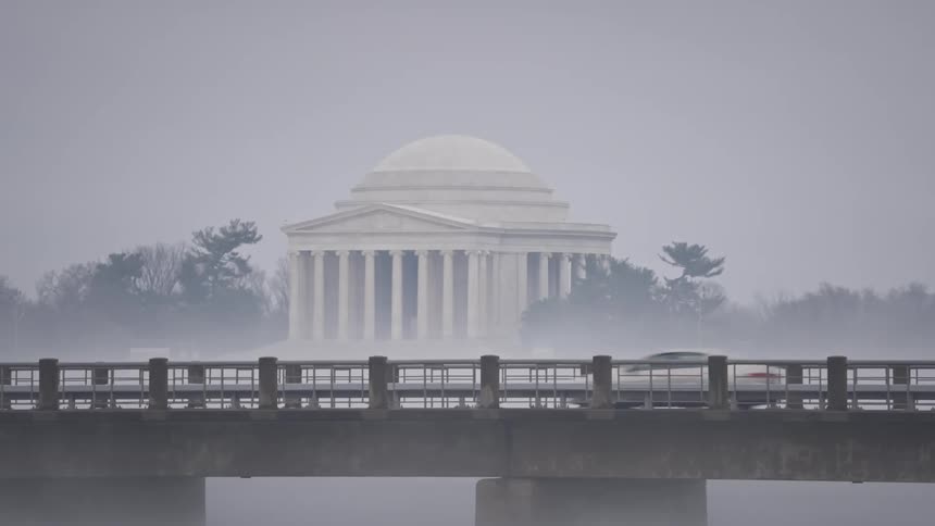 The jefferson memorial is visible through the fog behind a bridge with cars driving across it