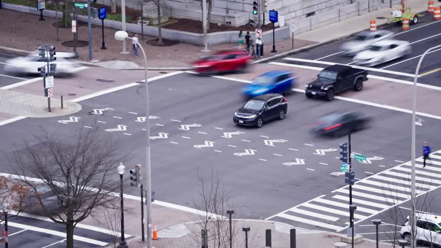 A busy city intersection with blurred vehicles crosswalks and pedestrians