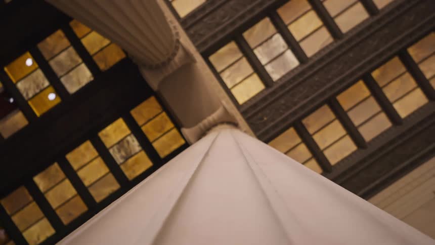 Looking upwards to a section of a coffered ceiling with ambertoned glass panels and the top portion of a fluted column