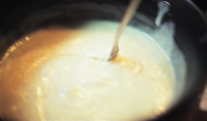 Fork with a piece of bread being dipped into melted cheese