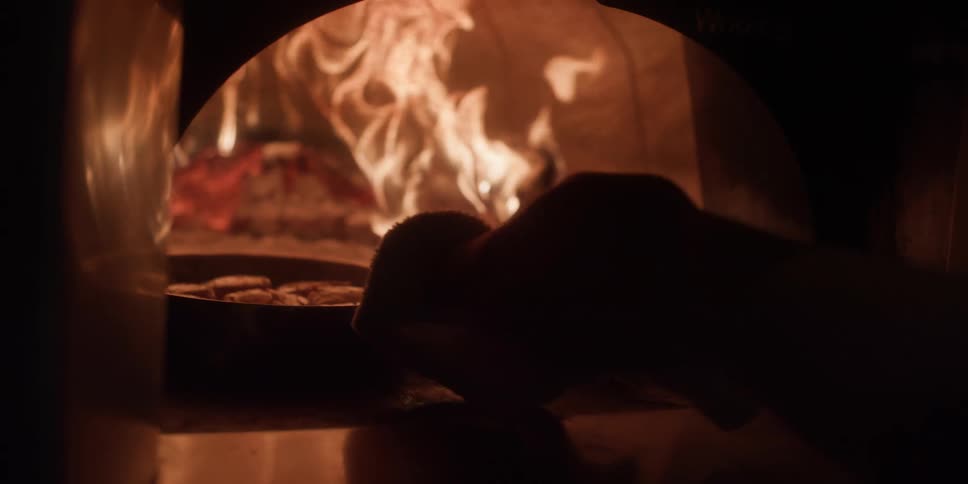 Man inserts a steaming skillet into a wood burning oven
