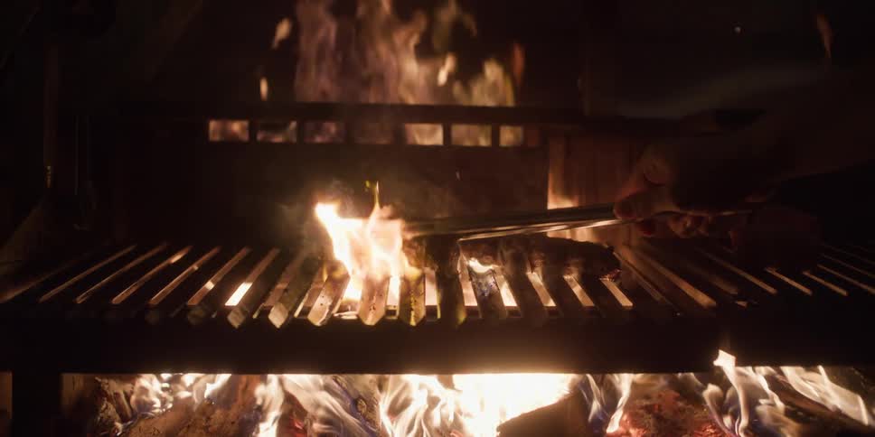 A hand holding tongs to turn or move the meat on the grill
