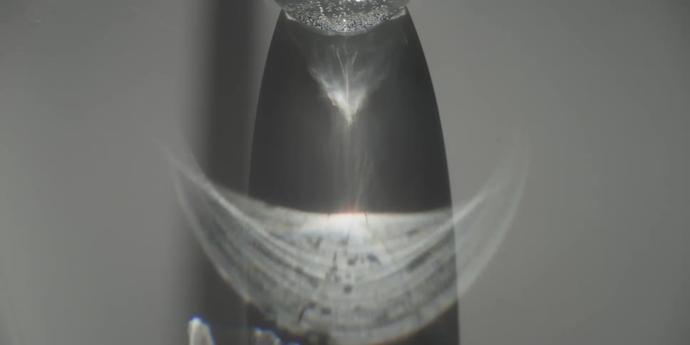 Closeup of water flowing from an obscured object indoors with light reflecting on the stream