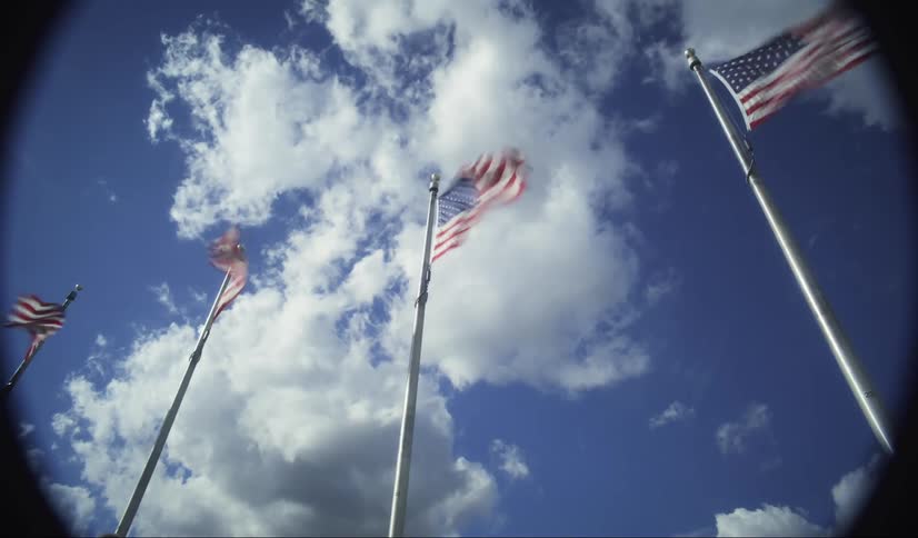 American flags wave in the wind against a bright blue sky with fluffy clouds framed by a circular lens