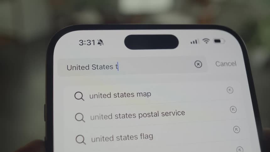 Someone is typing united states tariffs into a search bar on a smartphone