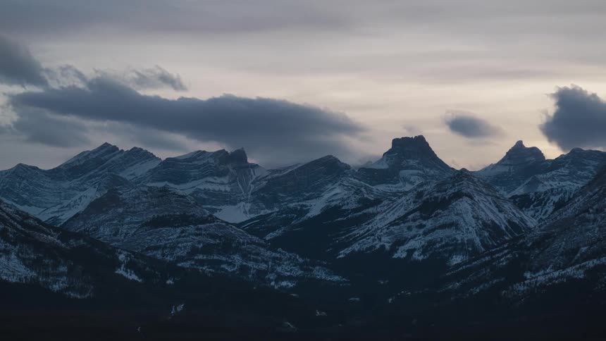 Aerial timelapse of a snow-covered mountain range and the valley below at sunset