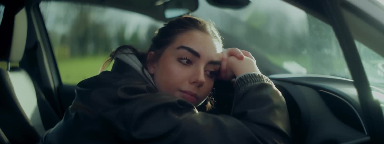 A woman is resting her head on the steering wheel of a car