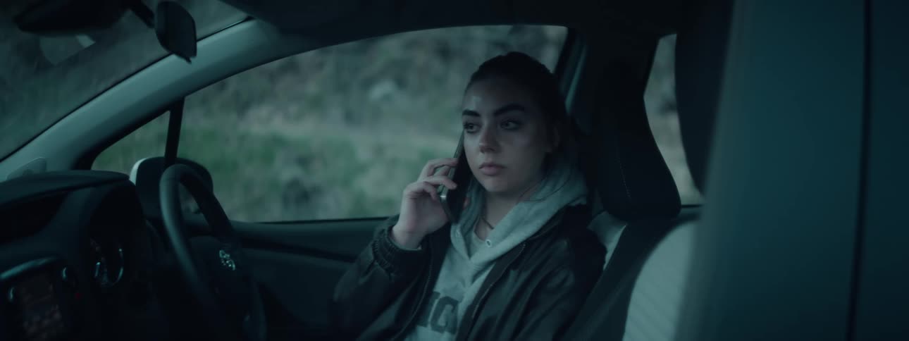 Woman frowns slightly while talking on a smartphone as she sits in a parked car