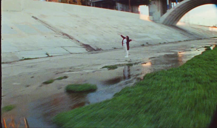 A woman is dancing between two bridges near a patch of grass in a canal