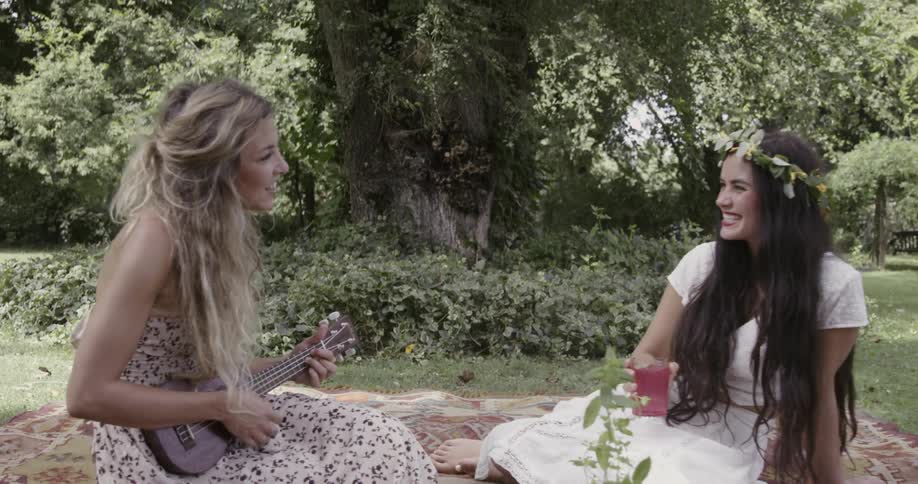 Two women in dresses smiling and having a picnic in park