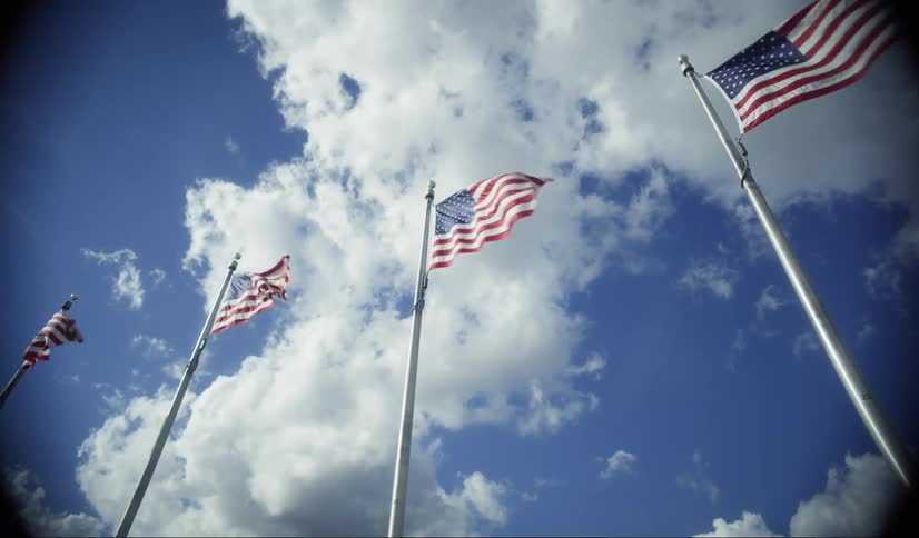 Four american flags wave from their poles against a partly cloudy blue sky