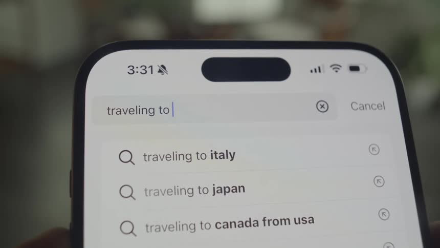 A closeup shot shows a smartphone screen displaying a search bar with the words traveling to europe and related search suggestions