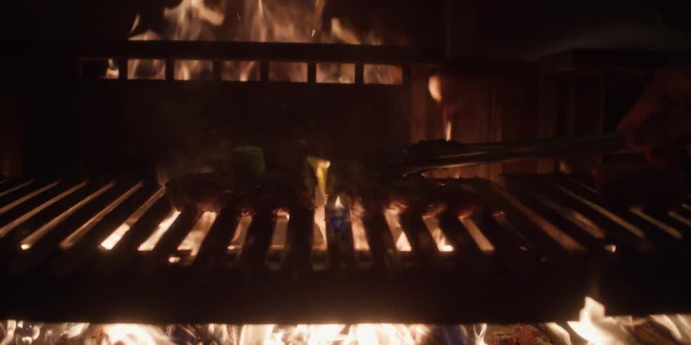 Person is cooking meat over a flame grill at night time