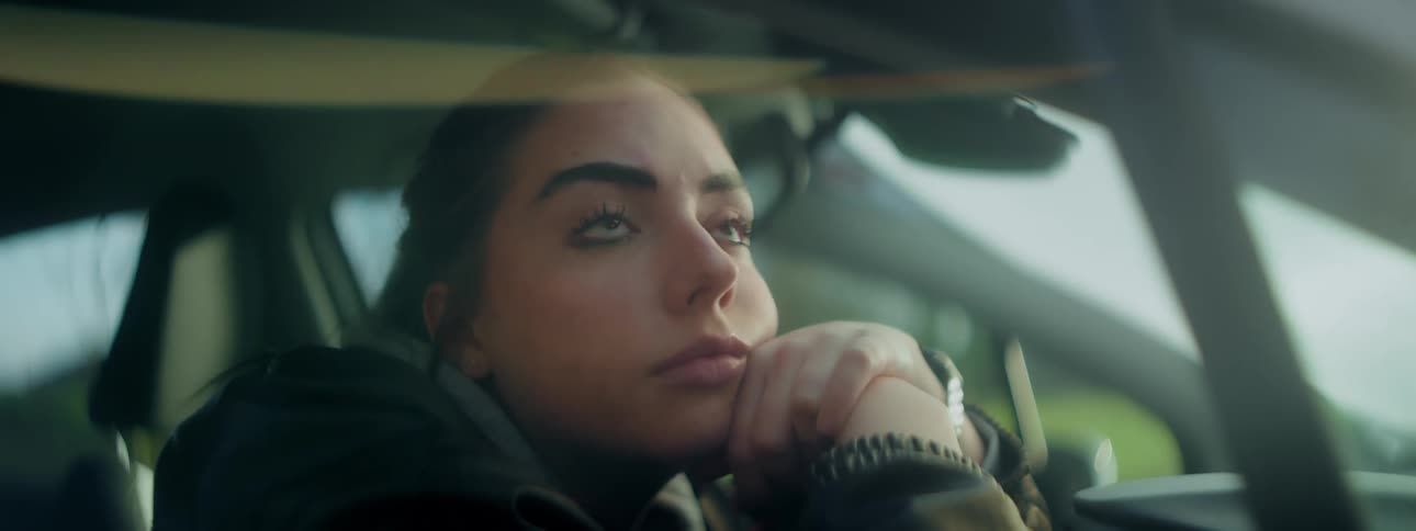 Woman sits in a stationary car and looks out a window during the day