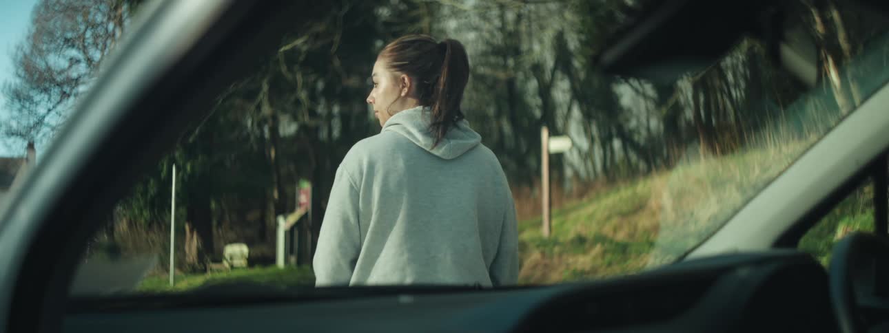 A woman looks around as she stands outside her car