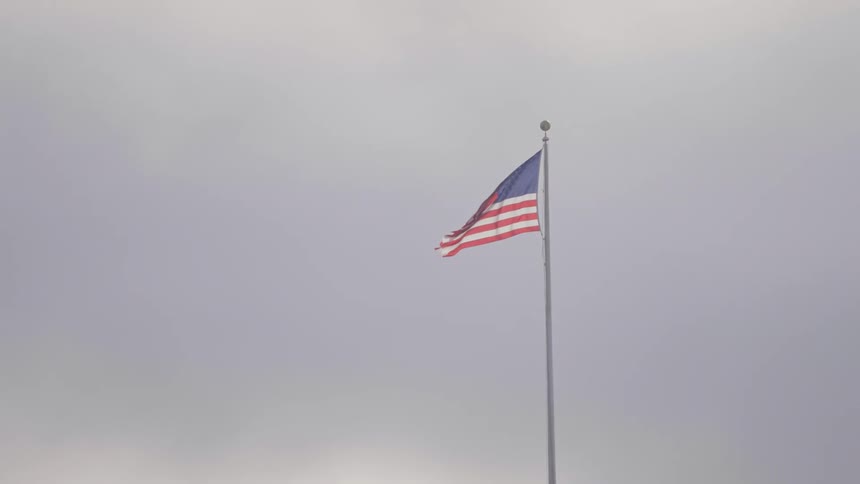 The american flag flies on a pole against a pale overcast sky