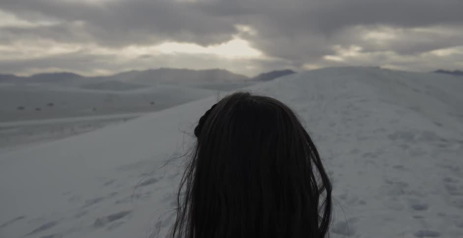 A woman is looking across an expanse of sand dunes under a dark sky