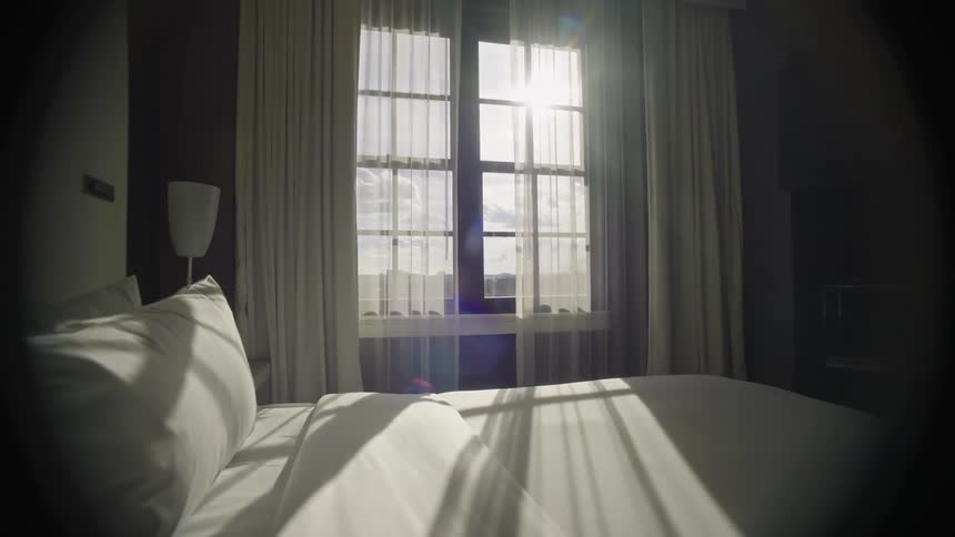 Sunlight streaming through a window onto a neatly made bed with white sheets on a clear day