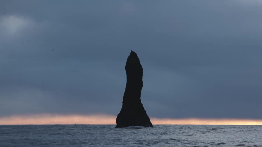 Birds fly around the large rock formation in the ocean