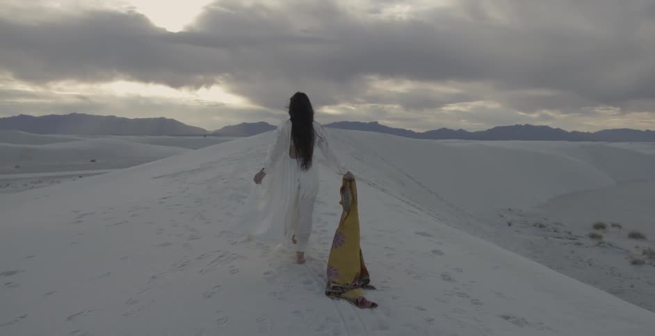 A woman walks across the sand dragging a colorful wrap