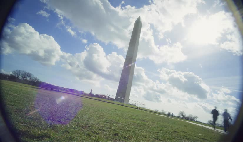 The washington monument rises tall against a cloudy sky and a green landscape