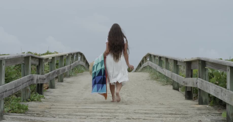 A woman carrying a beach towel and coconut walks up some stairs