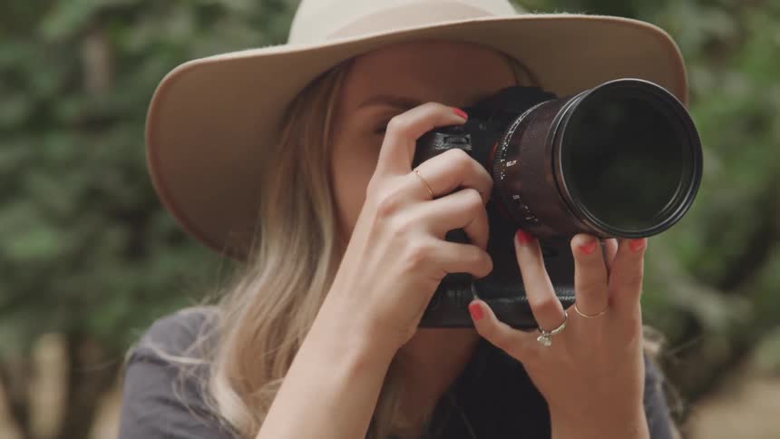 The face of a woman who has a smile on her face and is wearing a hat and then putting a camera in her face to take a picture