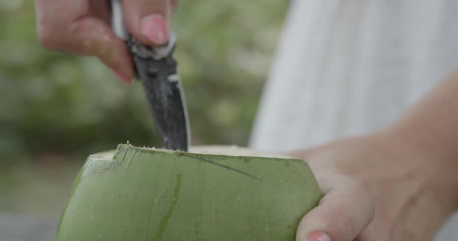 Woman cutting into a coconut with a knife
