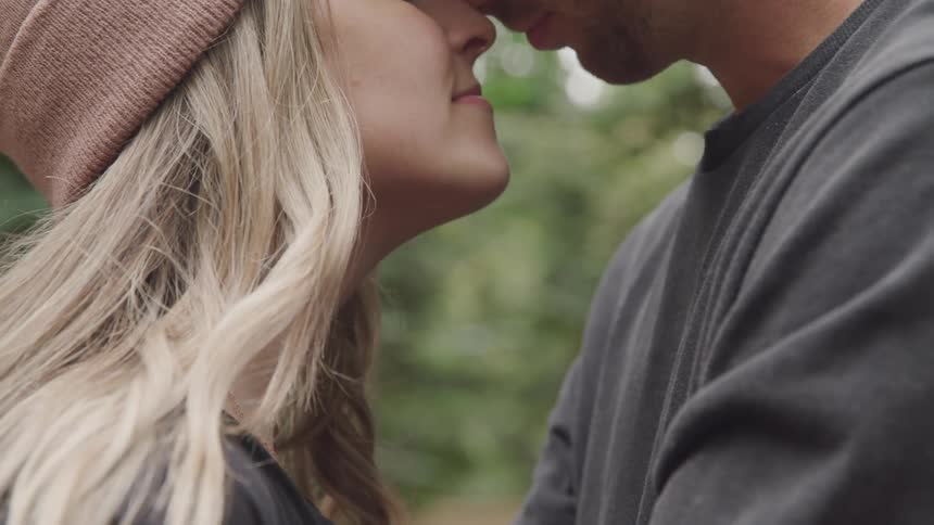 A young couple stands close together in an intimate moment their foreheads nearly touching as they share a tender connection in a natural outdoor setting