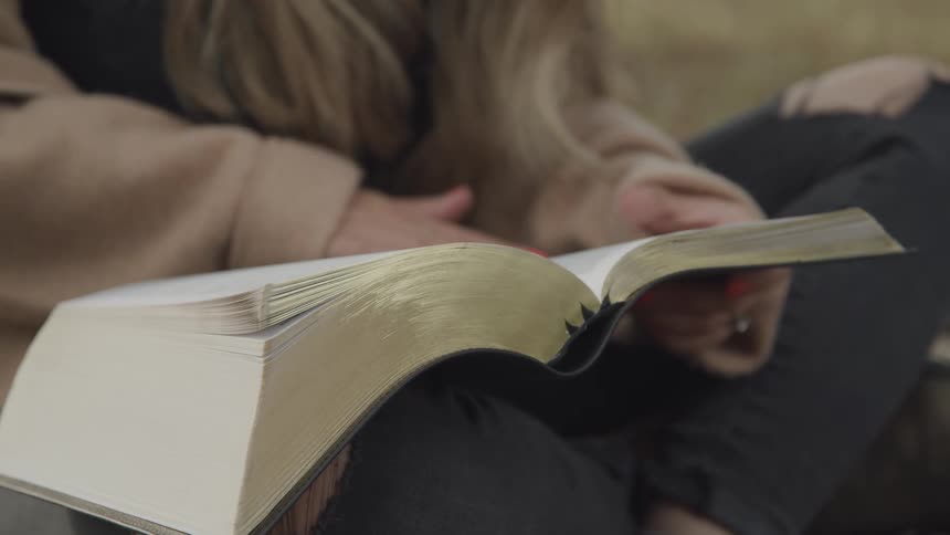 Blonde woman sits cross legged and flips through a book