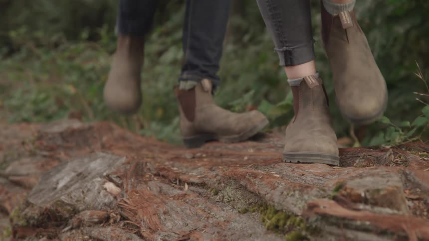 Two people wearing the same pair of brown leather boots walking in a forest environment