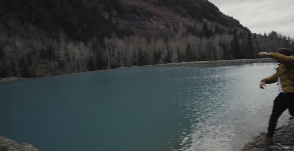 A man is skipping a stone across a lake and a woman is standing near him