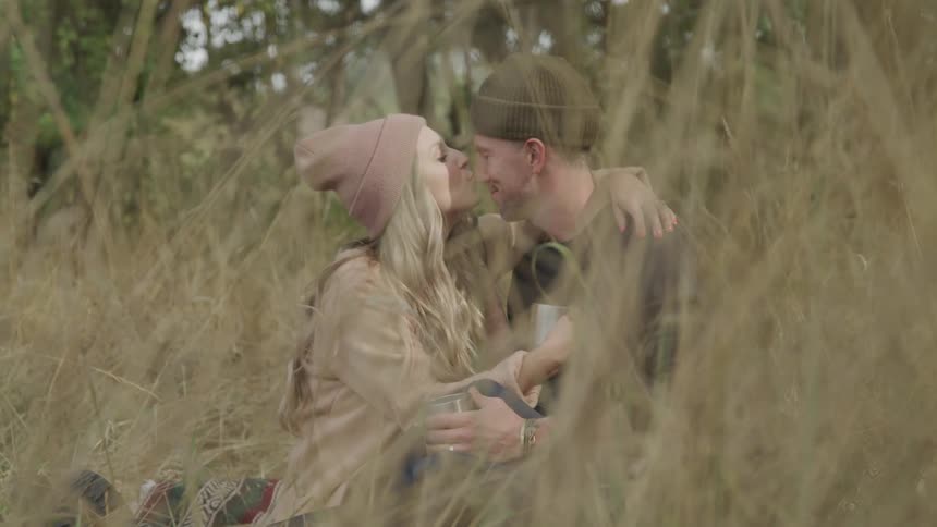 A couple sit in a field and kiss