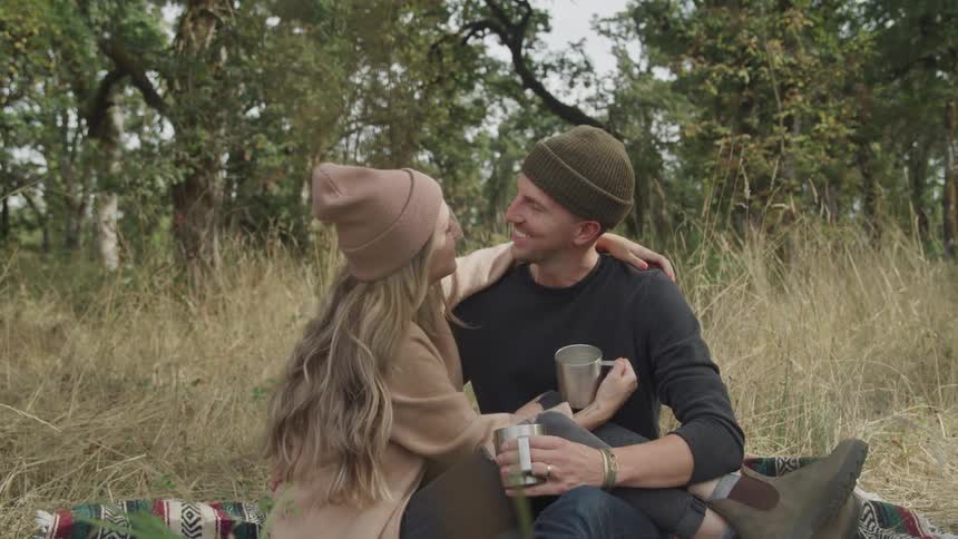 Happy couple sitting in a field with trees in the background and the man kissing her on the forehead