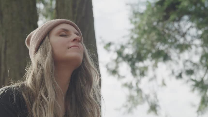 Woman with eyes closed looking up in the middle of a tree