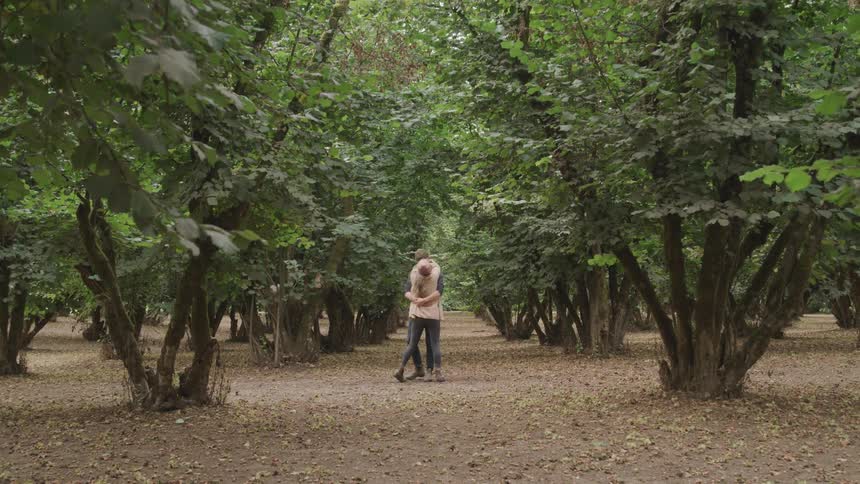 Couple running hand in hand through a valley with trees and hugging and kissing