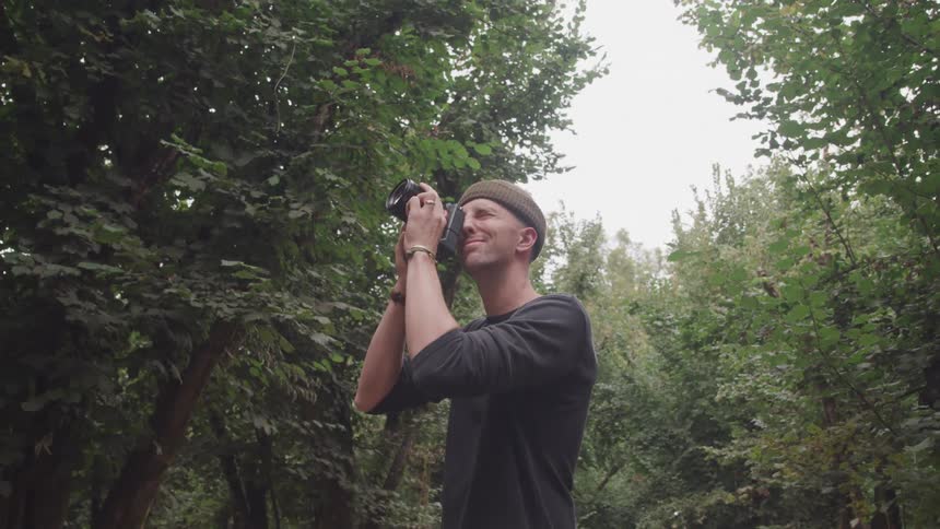 Man in the middle of a dense forest taking pictures with a professional camera
