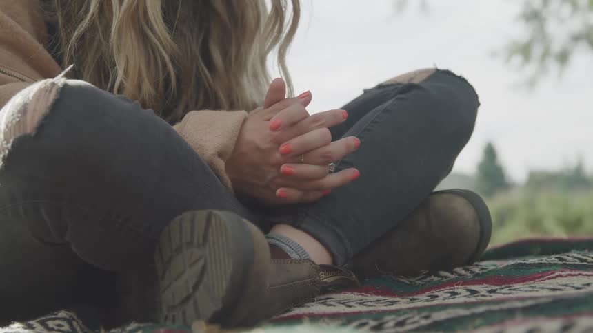 Close up of a pair of clasped hands of a woman sitting outdoors