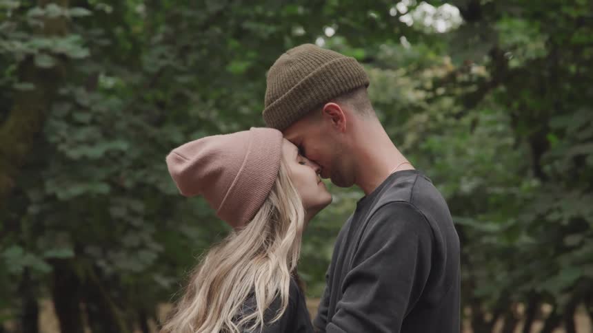 A couple embraces while standing face to face on a forest path surrounded by dense trees and lush foliage
