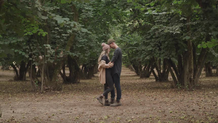A couple embraces while standing face to face on a forest path surrounded by dense trees and lush foliage