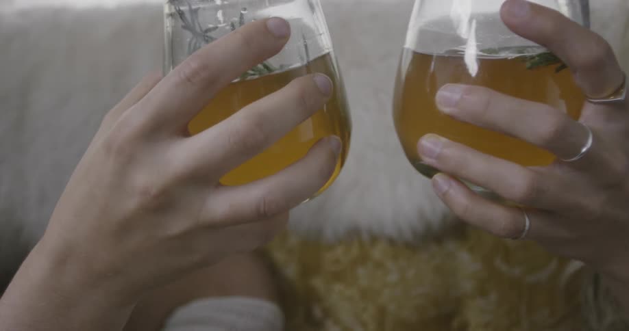 Two women cheersing wine glasses filled with yellow colored beverage