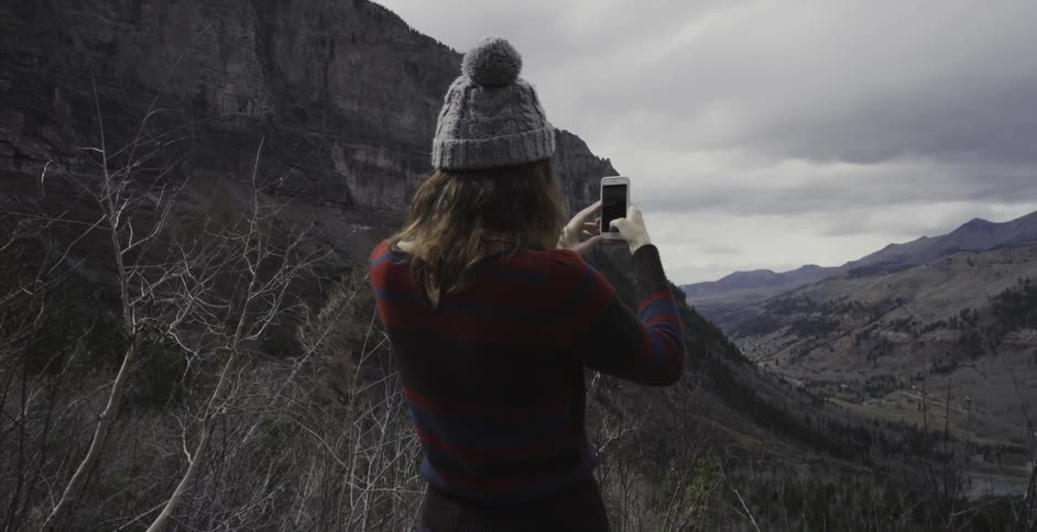 A woman is taking a photo of a mountain view on a cloudy day