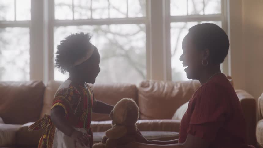 A mother is shaking a teddy bear in front of her daughter