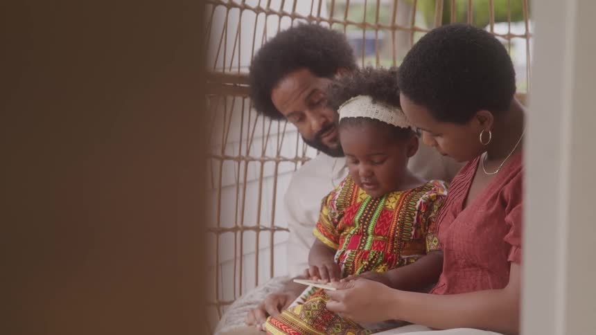 Father and mother sitting with their young daughter interacting with a book