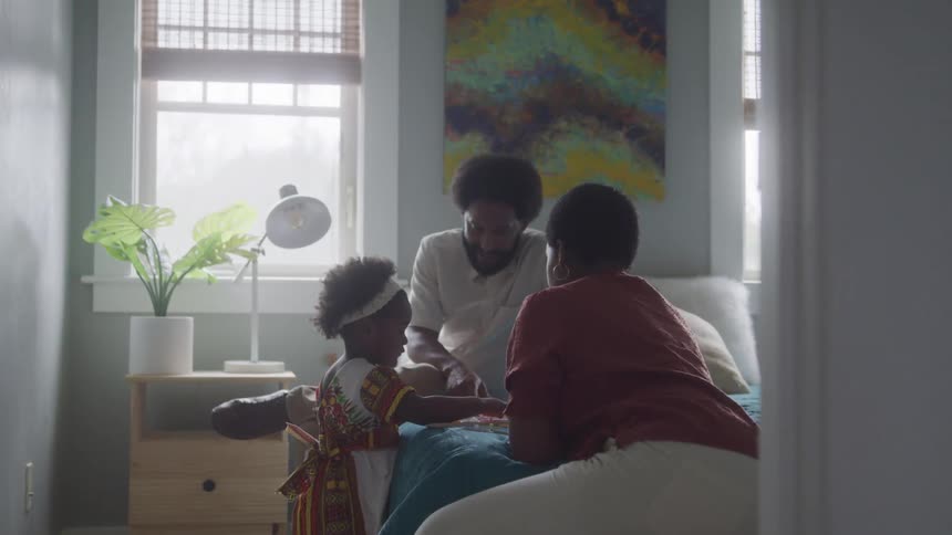 A man and a woman are sitting on a bed and playing with a little girl who is standing and fiddling with something on the bed