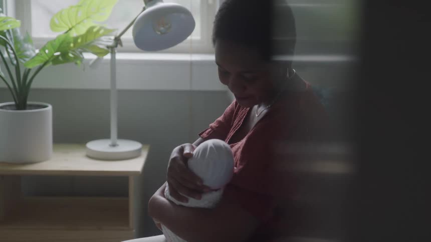 Mother caresses her infant and smiles while sitting near the window