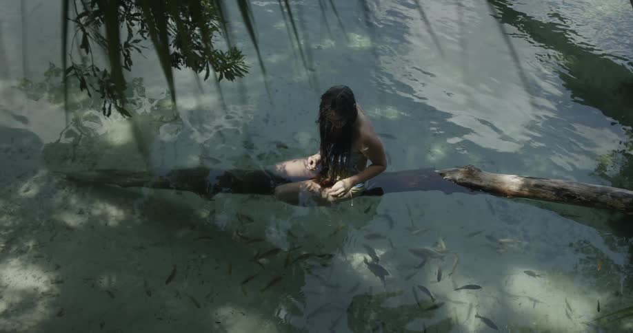 A woman sits on a submerged log watching the fish